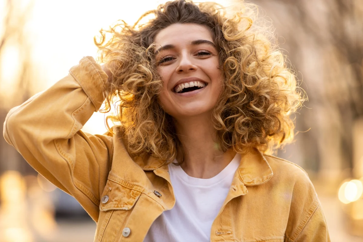 Junge Frau trägt blondes mittellanges Haar mit Locken